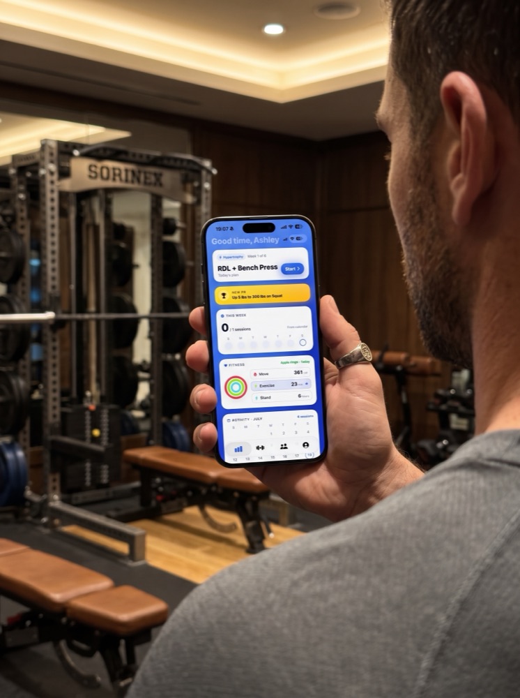 Client in a gym holding an iPhone running the Topset training app with the day's lifts queued up