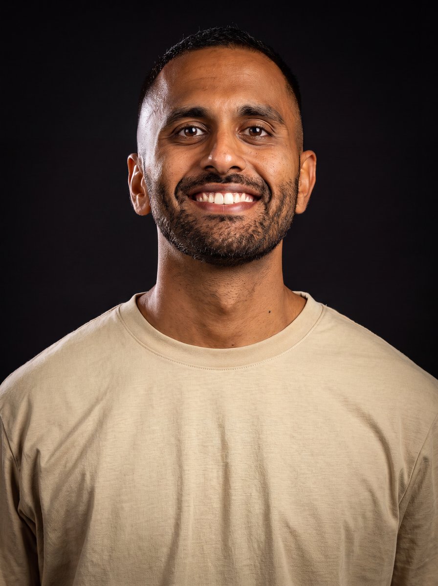 Rahul Ramesh smiling, studio portrait on a dark background